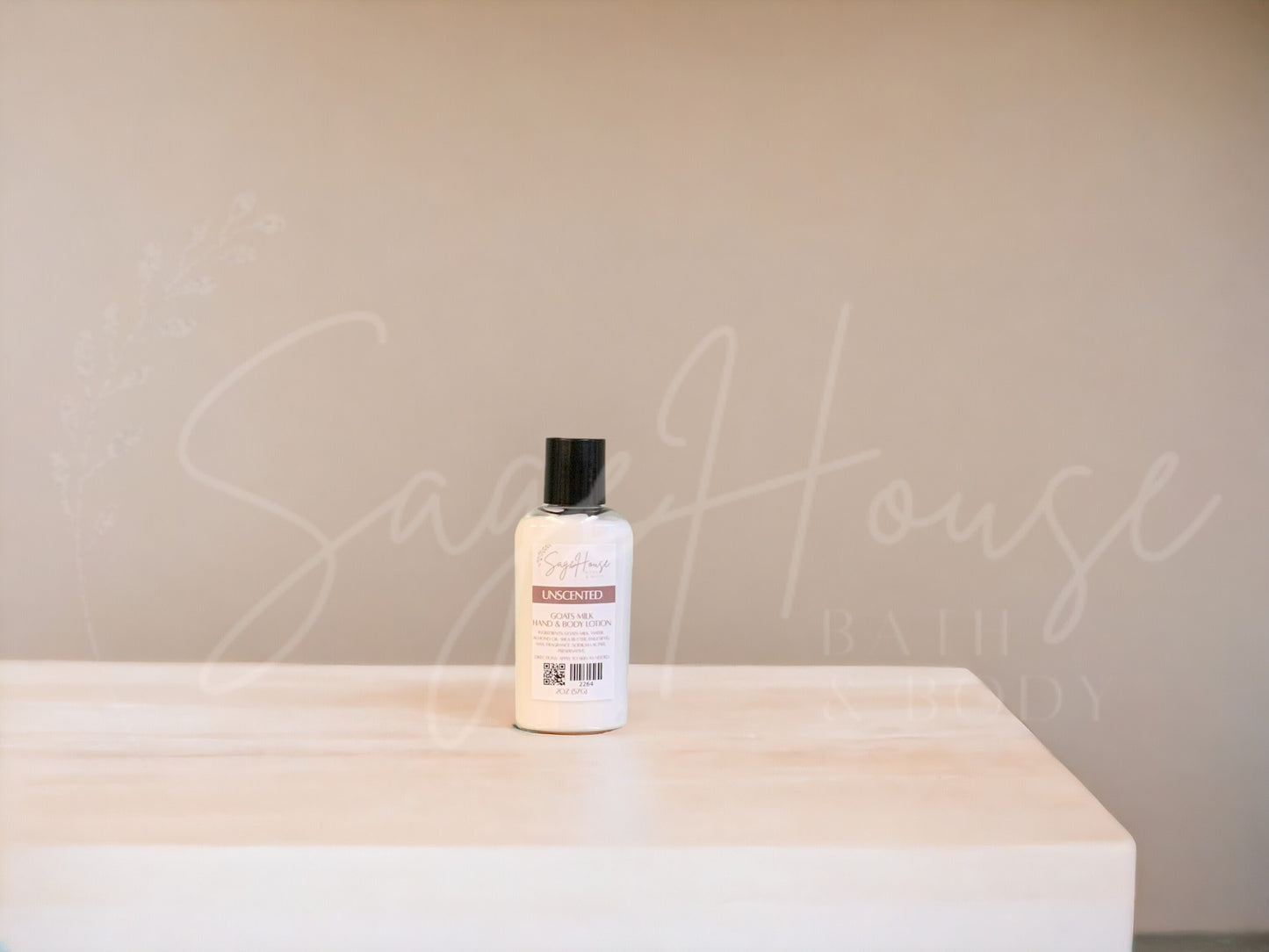 A small bottle of lotion, sitting on a light wood surface, with a tan background. Has SageHouse logo inlayed