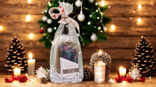 A round gift sack containing various bath and body products, tied with a ribbon. sitting on a wood surface with christmas decor in background