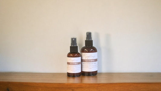 Amber colored spritz bottles in two sizes, both with soothing labels, on wood surface. sold individually.