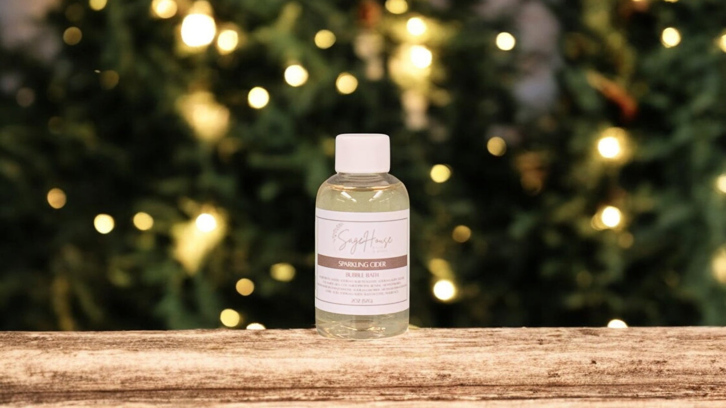 A small bottle of bubble bath, with white lid. On a wood top with greenery in the background.