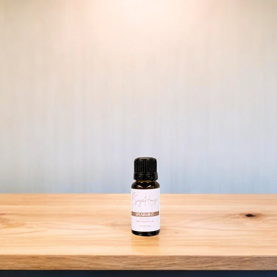 A small bottle of spearmint essential oil is placed on a wooden surface with a plain background.