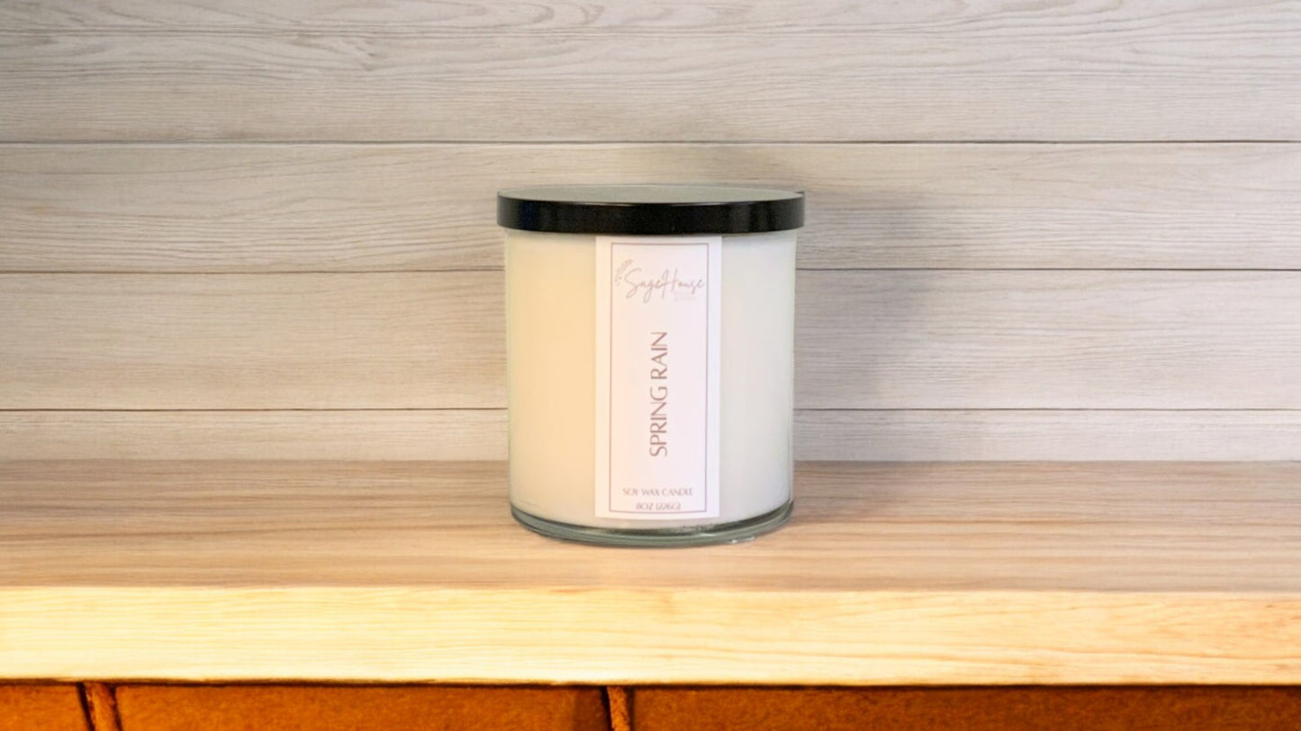 A white soy wax candle in a clear container, placed on a wooden surface, with a label on the front.