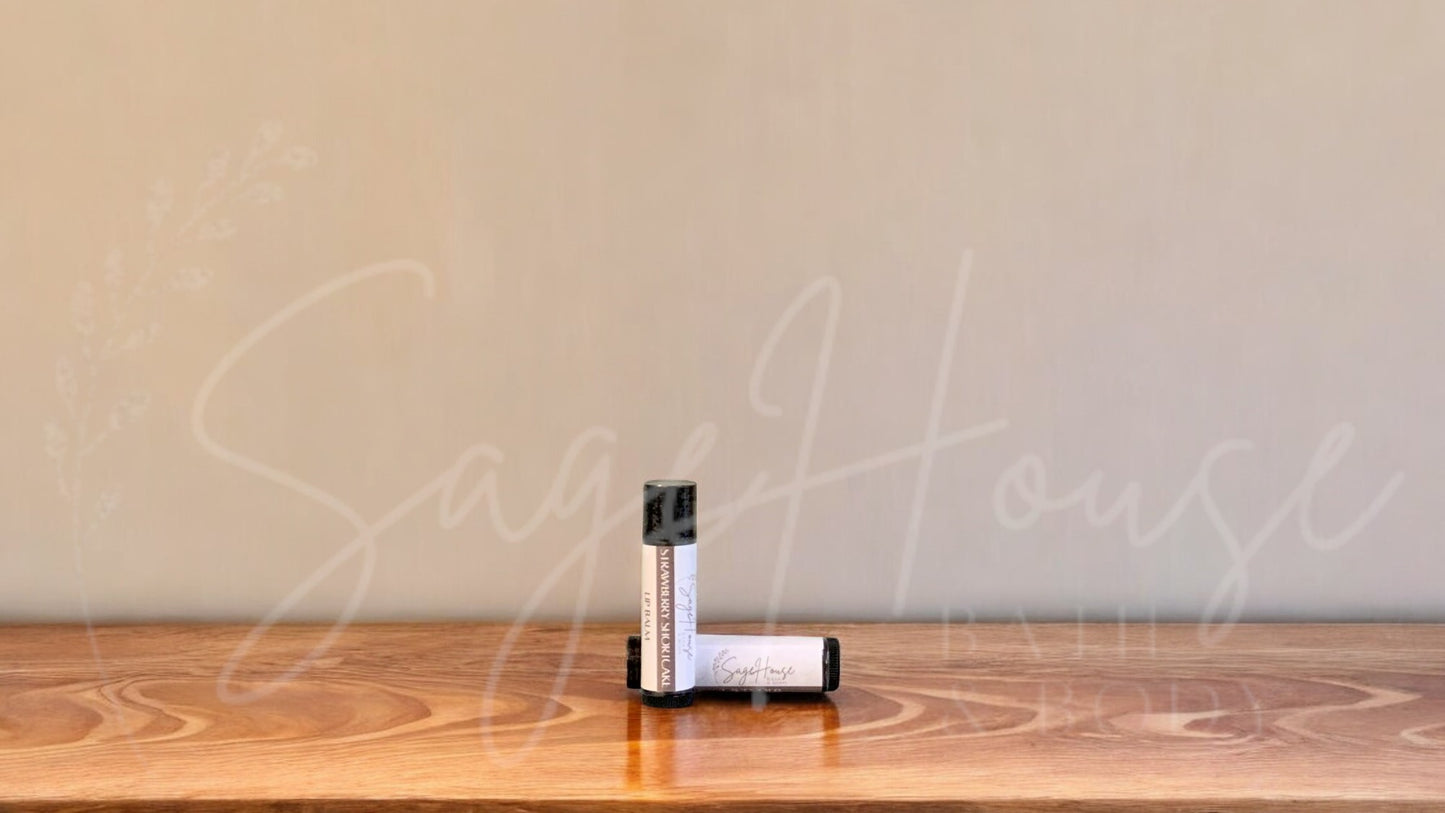 A tube of strawberry shortcake lip balm placed upright with a tube lying behind it, on a wooden surface.