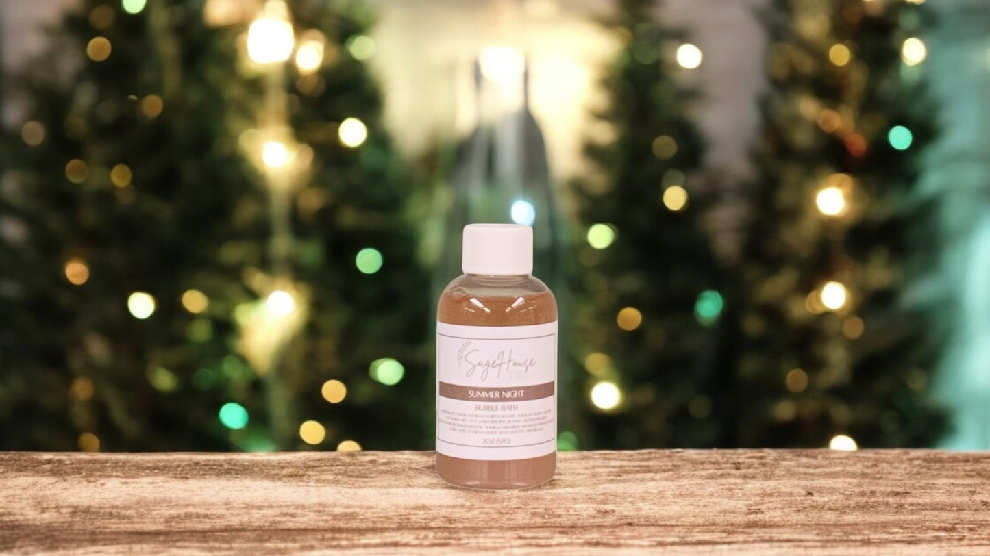 A small bottle of bubble bath, with white lid. On a wood top with greenery in the background.