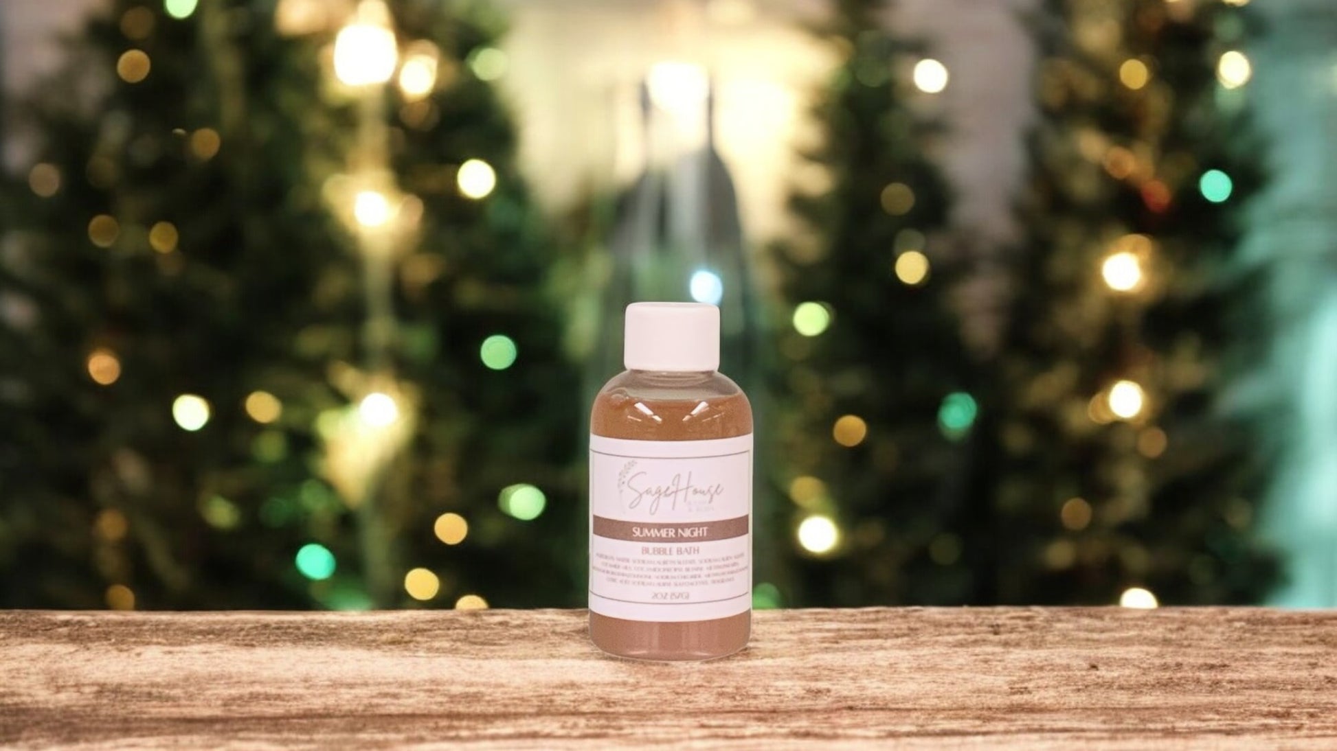 A small bottle of bubble bath, with white lid. On a wood top with greenery in the background.