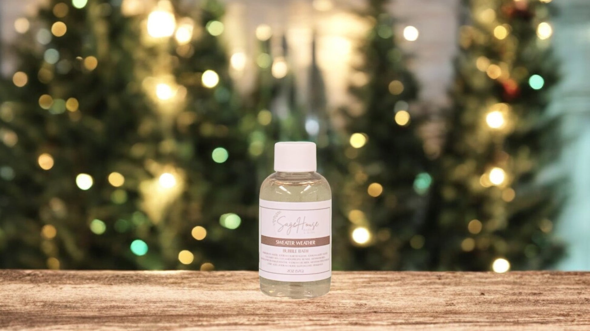 A small bottle of bubble bath, with white lid. On a wood top with greenery in the background.