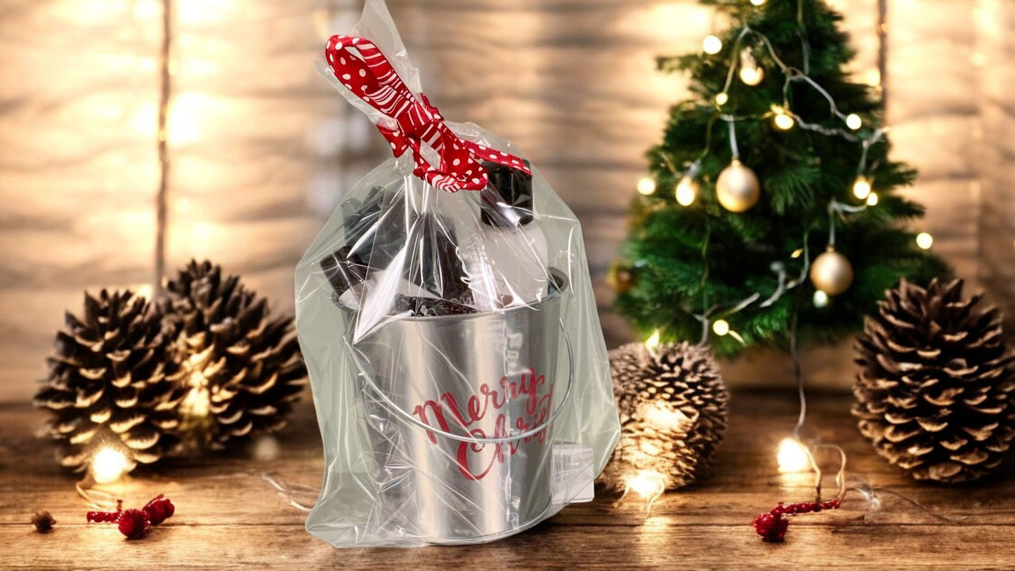 A christmas tin containing various bath and body product, packaged in a bag and tied with a red ribbon. on a wood surface with christmas theme in background.
