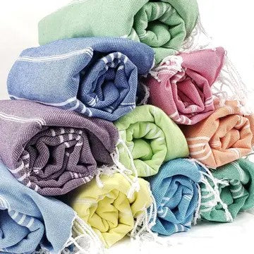 Variety of colors of Turkish cotton towels, all rolled up and stacked, on a white background.