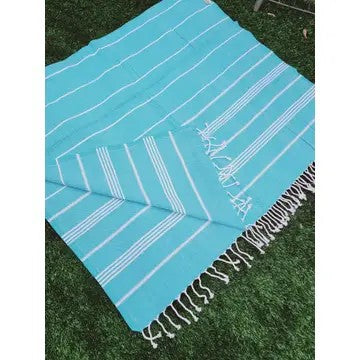 Turquoise Turkish cotton towel, folded onto itself, on grass, on a white background.