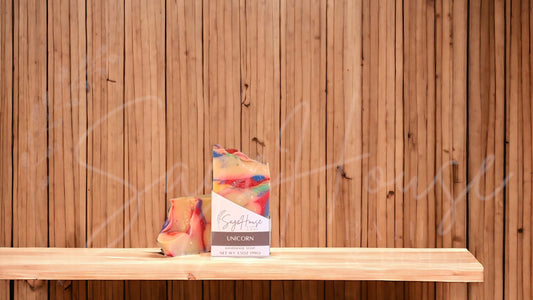 A white bar of soap with rainbow accents of red, blue, yellow, orange, green and purple in a white labeled box, on a wood surface.