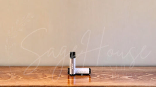 A tube of vanilla lip balm placed upright with a tube lying behind it, on a wooden surface.