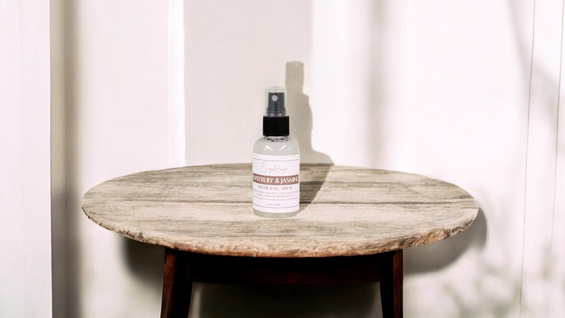 A clear bottle with black spritz top. sitting on a stone table with a white wall in the background