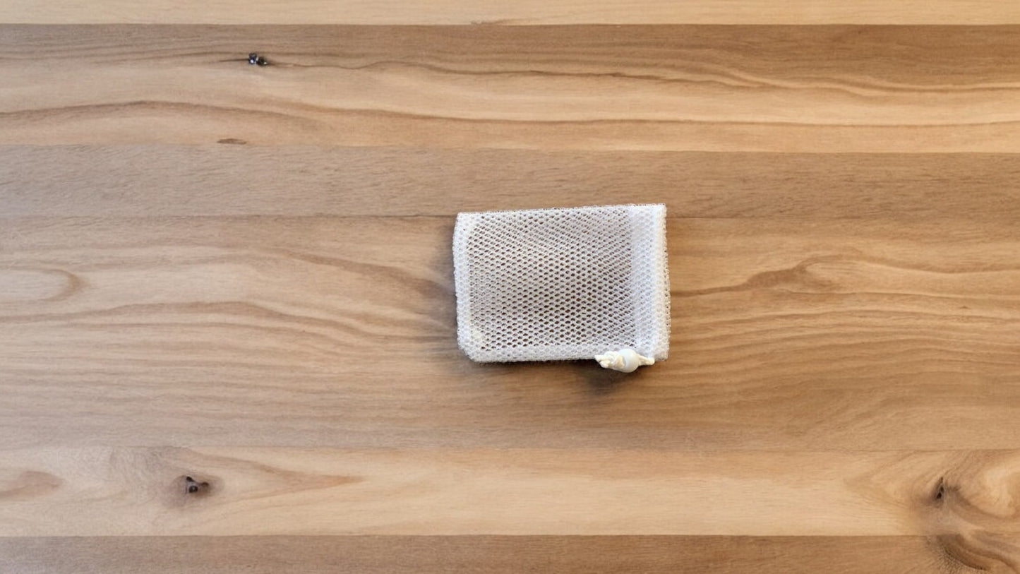 A Soap Scrub Pouch in white, placed on a wooden surface.