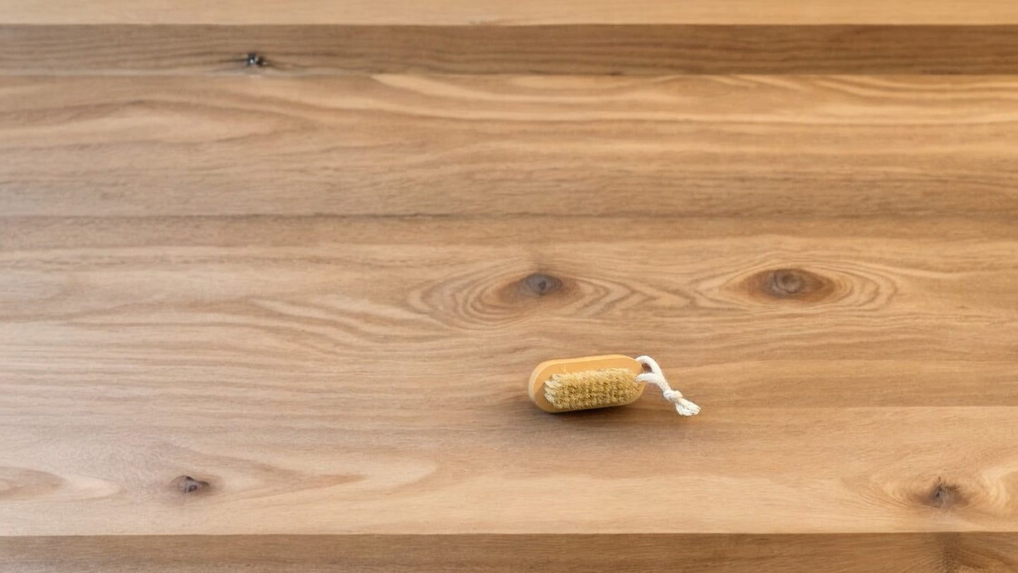 A nail brush with a wooden handle placed on a wooden surface.