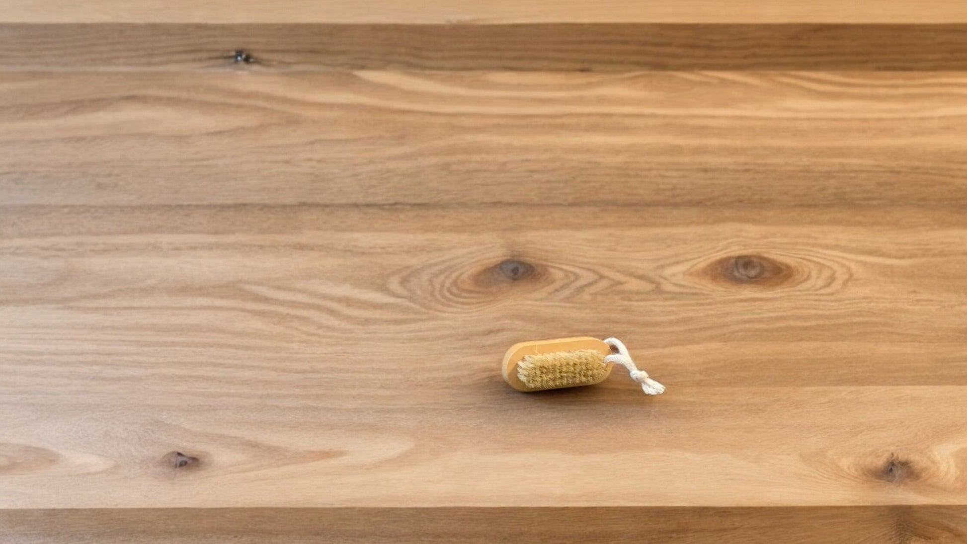 A nail brush with a wooden handle placed on a wooden surface.