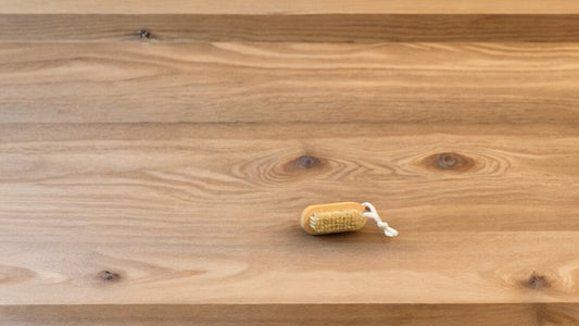 A nail brush with a wooden handle placed on a wooden surface.