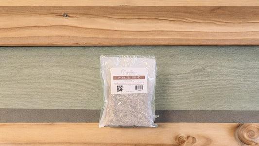 A large tea back in packaging, sitting on a wood surface with a sage colored background